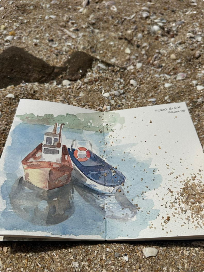 Watercolor sketchbook on the sand with two small boats on the water