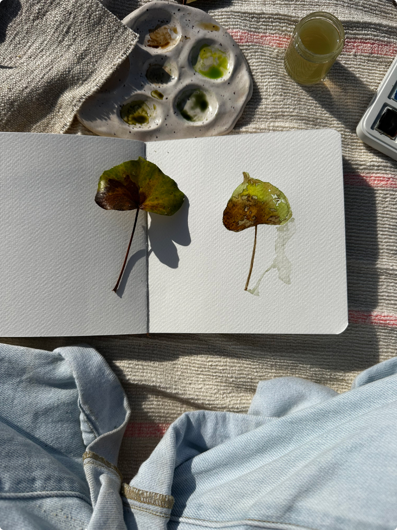 Sketchbook with two painted autumn leaves, next to a watercolor palette